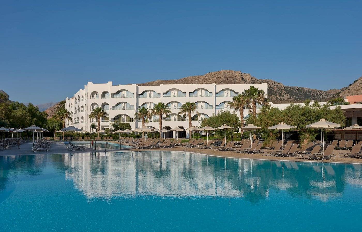 Außenpoolbereich des Atlantica Kalliston Resorts mit weißen Gebäuden und vielen Sonnenliegen.