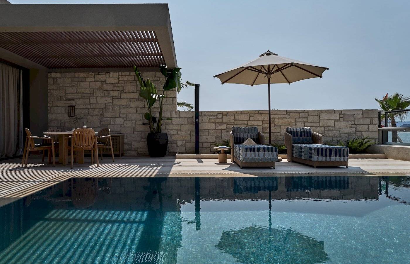 Terrasse des Atlantica Kalliston Resorts mit Sonnenschirm und Sesseln neben einem Pool.