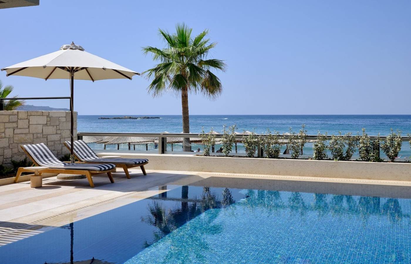 Pool-Terrasse des Atlantica Kalliston Resorts mit Blick auf das Meer und Sonnenschirmen.