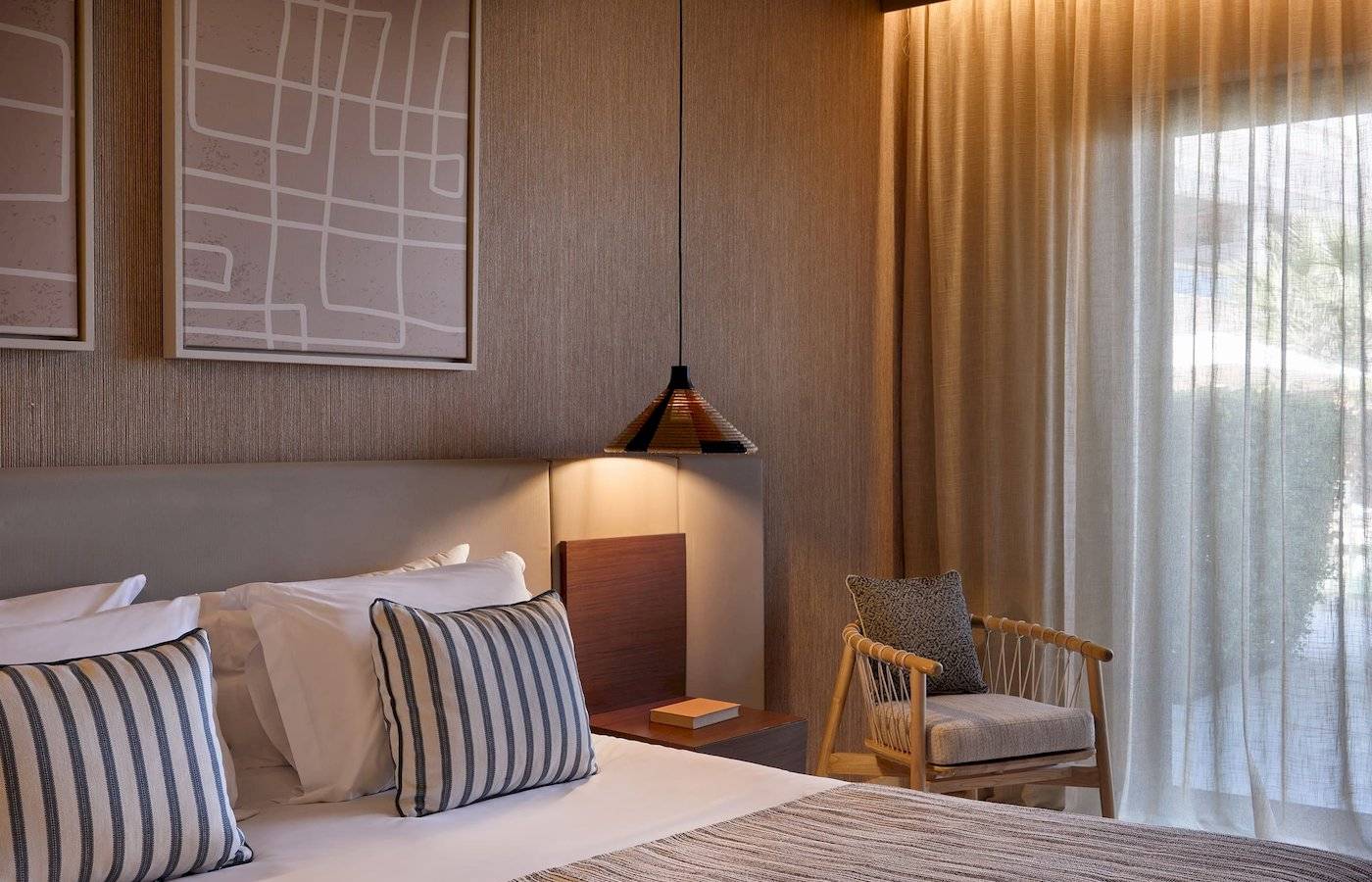 Ein elegantes Hotelzimmer mit Doppelbett, Kissen, Nachttisch und hängender Lampe im Atlantica Kalliston Resort.