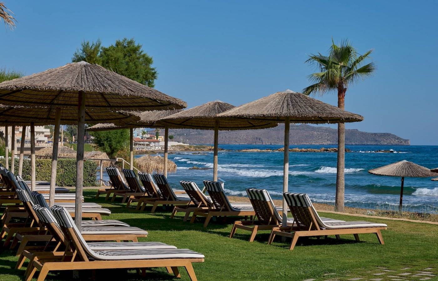 Strandliegen unter Strohhüten am Atlantica Kalliston Resort mit Blick auf das Meer.