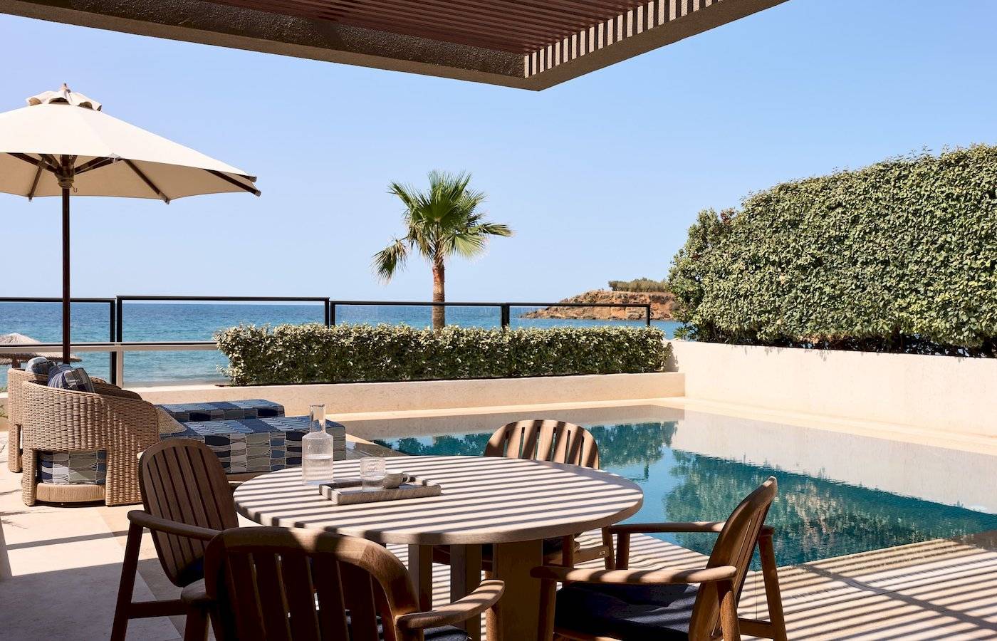 Terrasse mit Meerblick im Atlantica Kalliston Resort mit Tisch, Stühlen und Sonnenschirm.