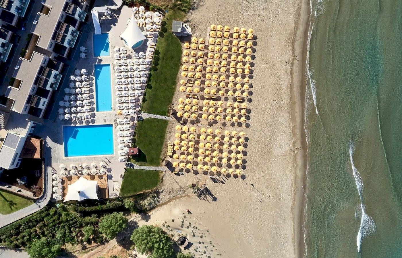 Atlantica Kalliston Resort, Blick auf das Hotel am Strand mit Pool und vielen Sonnenschirmen.