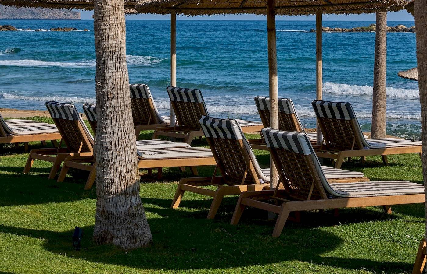 Strand-Lounge-Stuhle unter Palmenbaumen am Atlantica Kalliston Resort.