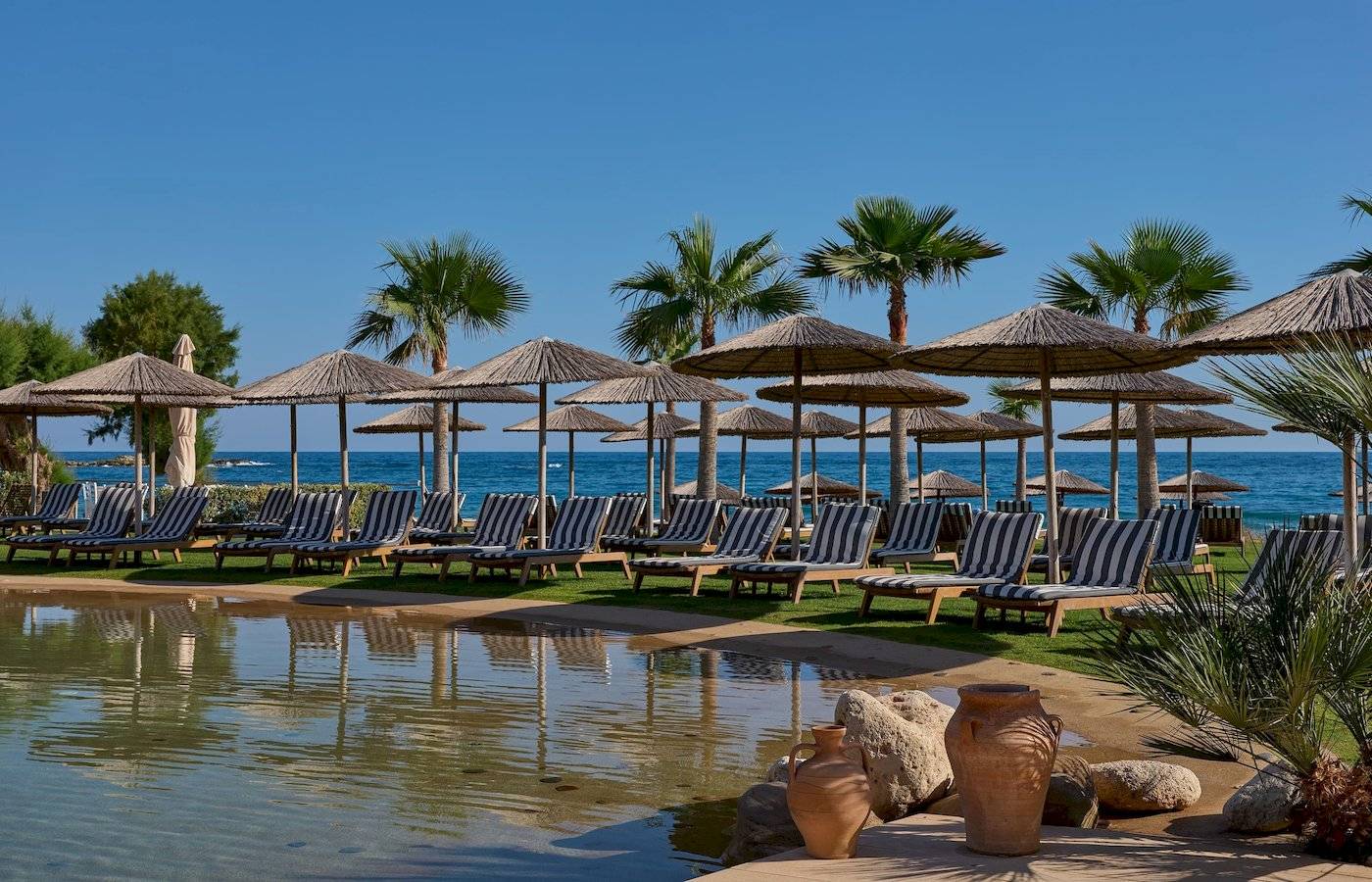 Atlantica Kalliston Resort Strand mit Lounge-Stühlen und Sonnenschirmen