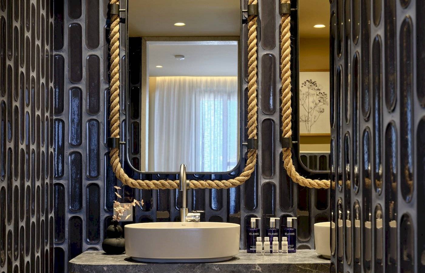 Badezimmer des Atlantica Kalliston Resorts mit schwarzer Fliesenwand und Spiegeln, die mit Seilen verziert sind.