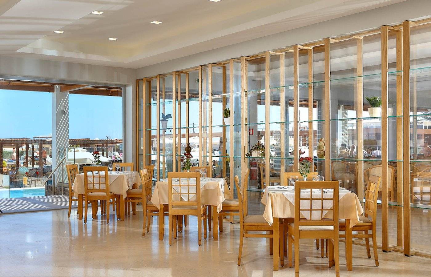 Innenbereich des Astir Beach Hotels in Kreta mit geräumigen Tischen und Stühlen, Glaswänden und Aussicht auf den Pool.