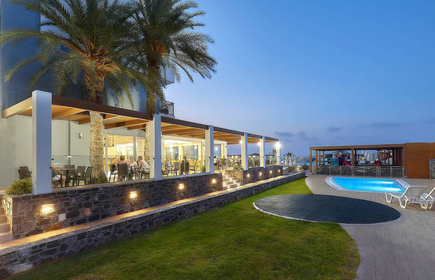 Terrasse des Astir Beach Hotels auf Kreta bei Abendbeleuchtung mit Palmen und Pool.