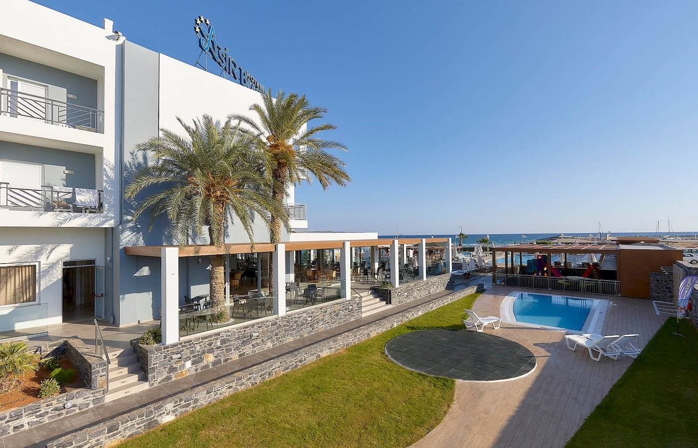 Außenansicht des Astir Beach Hotels auf Kreta mit Swimmingpool, Palmen und Terrasse.