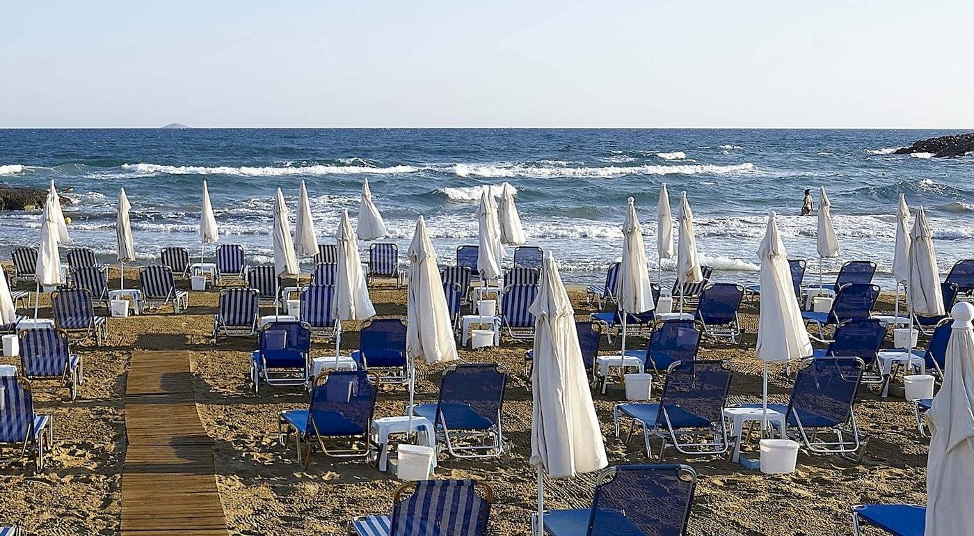 Strand des Astir Beach Hotels in Kreta mit vielen blauen Liegen und Sonnenschirmen.