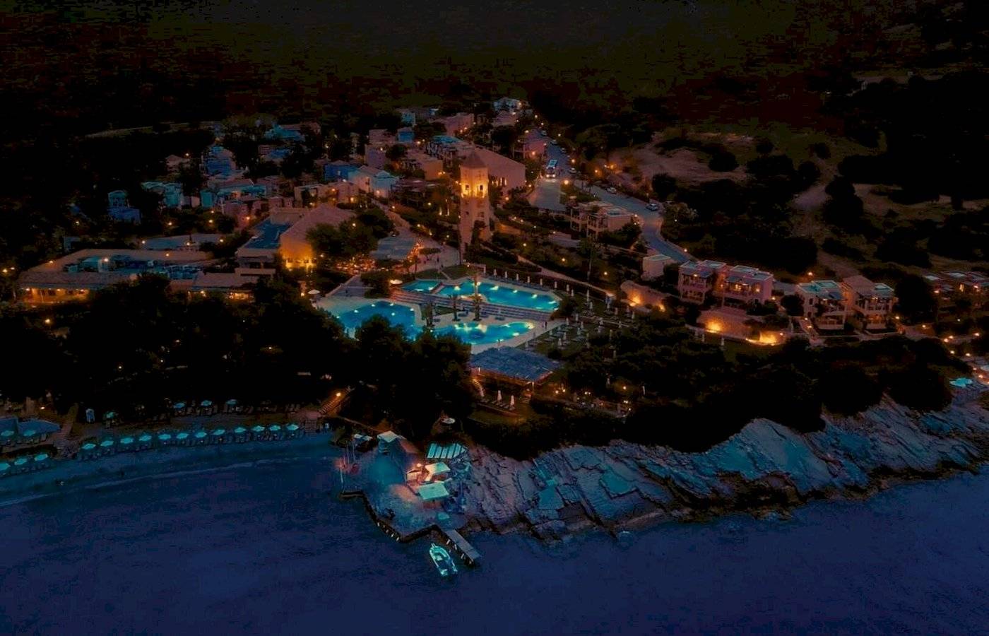 Nachtansicht des Candia Park Village Hotels mit beleuchteten Gebäuden und Pools