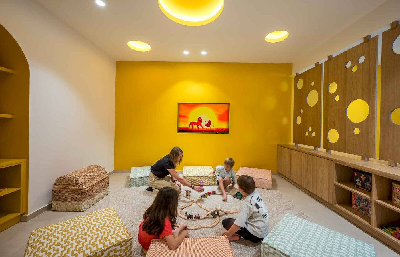 Arminda Hotel Kinderspielzimmer mit gelben Wänden, Holzmöbeln und Spielen.