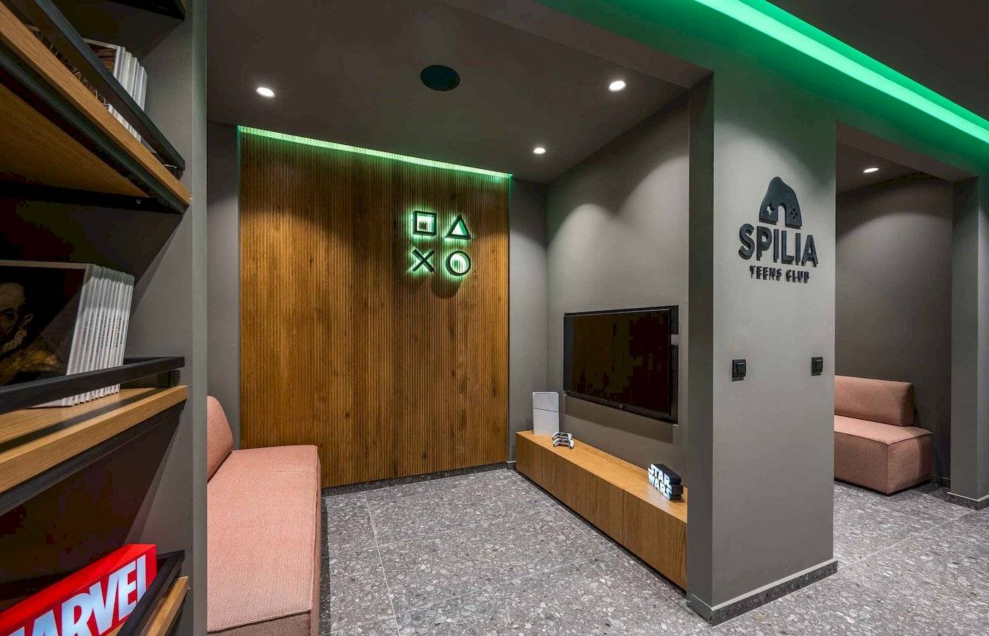 Innenbereich des Spilia Teens Club mit einer Couch, einem Fernseher und einem Regal mit Büchern.