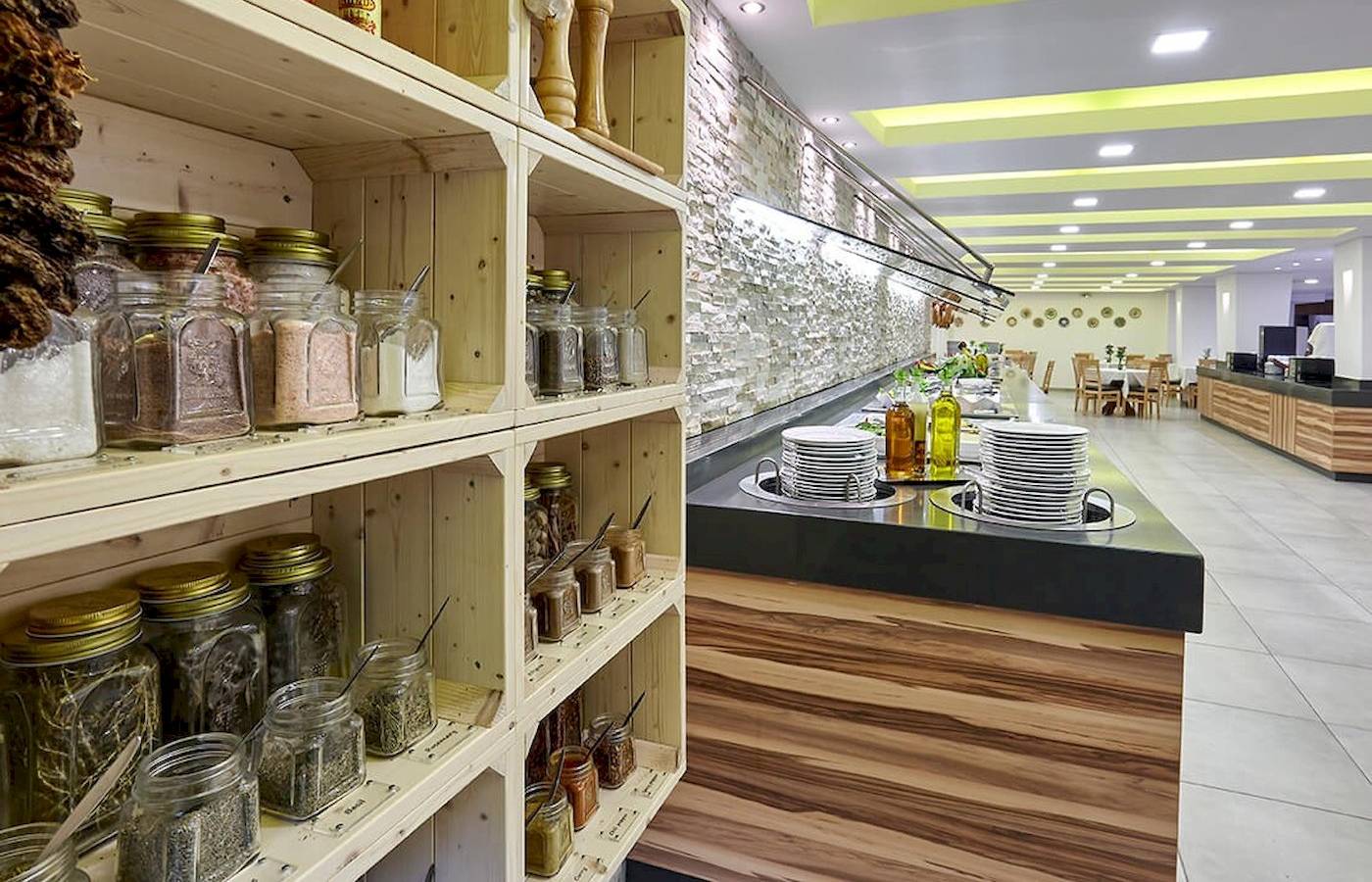 Innenbereich des Arminda Hotel & Spa mit Regalen voller Gewürzgläser und einer Theke mit gestapelten Tellern.