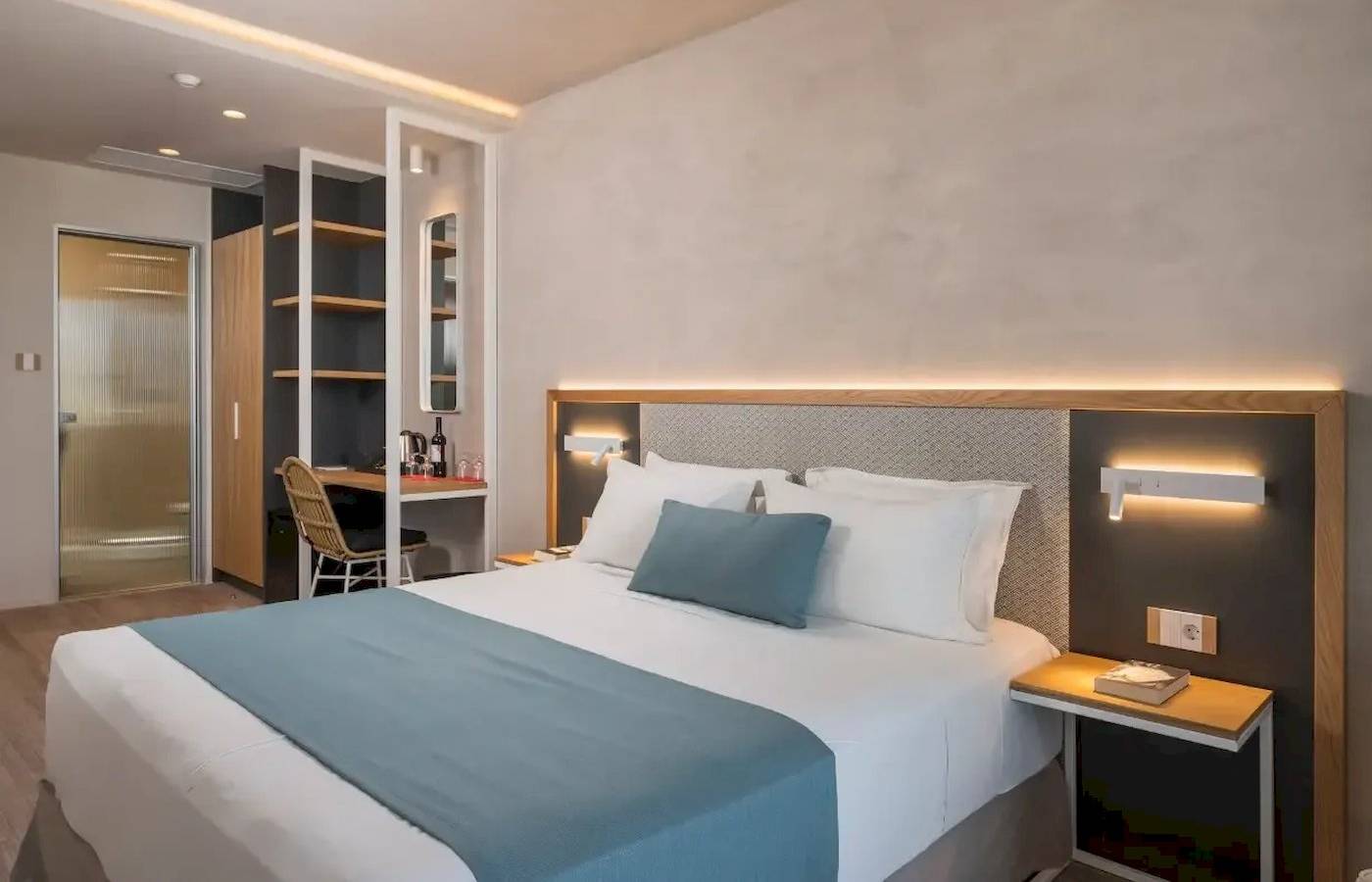 Inneneinrichtung eines Zimmers im Corissia Beach Hotel mit Bett, Schreibtisch und Wandbeleuchtung.