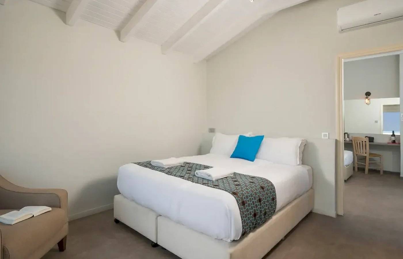 Schlafzimmer im Corissia Beach Hotel mit weißem Bett, blauem Kissen und Klimaanlage.