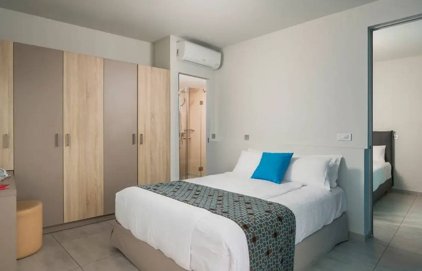 Innenansicht eines Zimmers im Corissia Beach Hotel mit einem Bett, Kissen, Decken und Holzschränken.