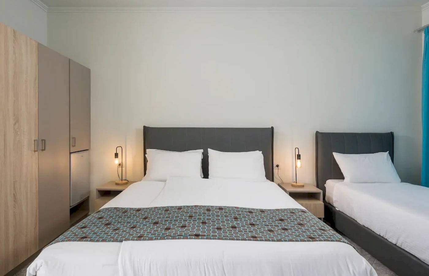 Zweibettzimmer im Corissia Beach Hotel mit zwei Betten, weißen Laken, Kopfkissen, Nachttischen und Lampen.