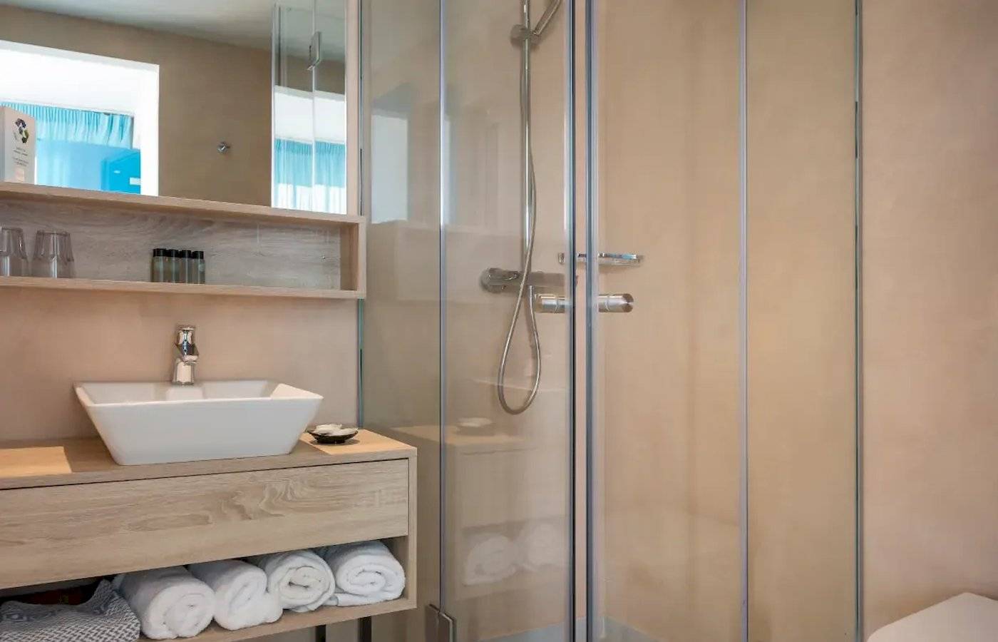 Badezimmer im Corissia Beach Hotel mit Glasdusche, Waschbecken und Handtüchern