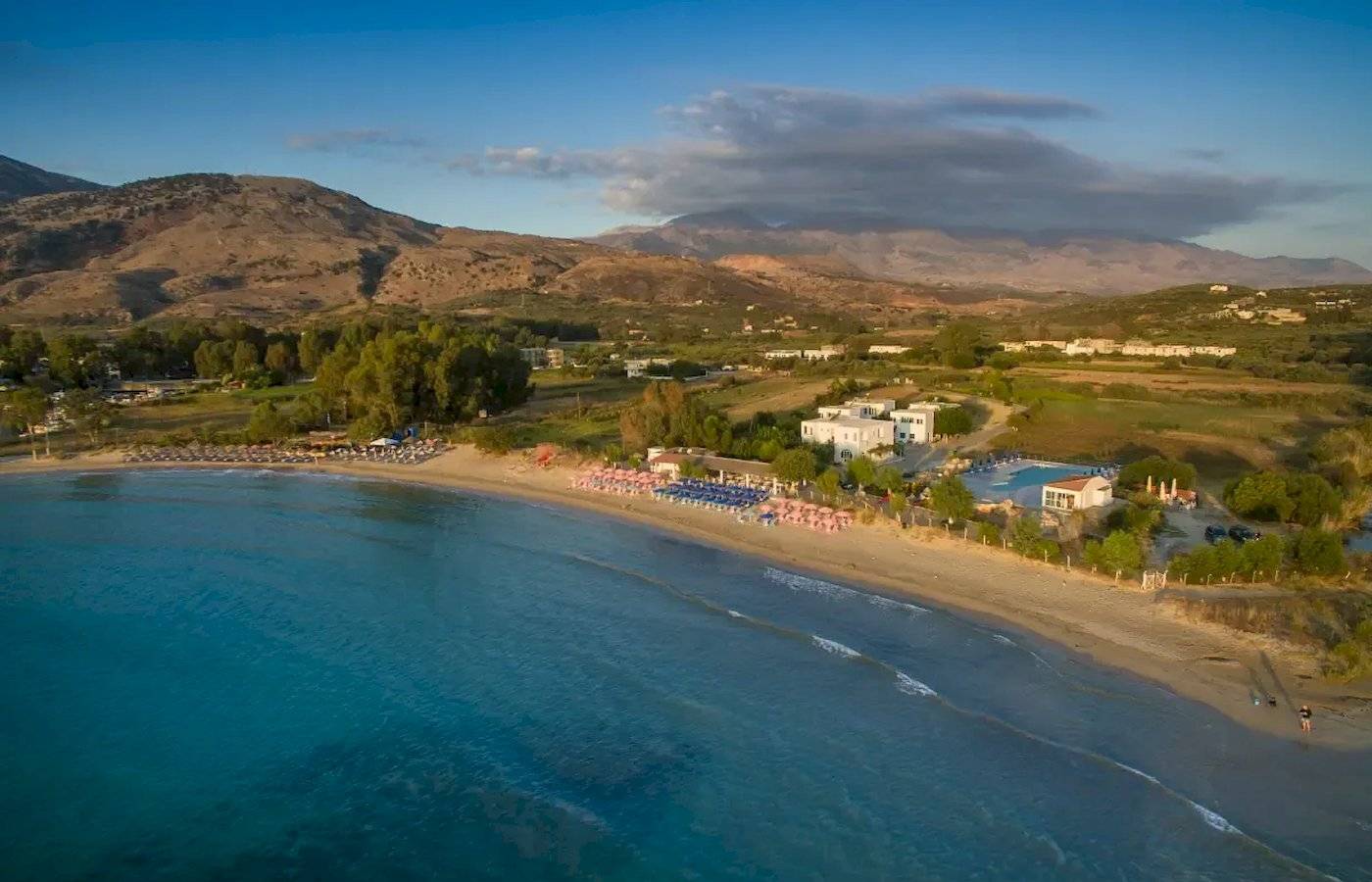 Luftaufnahme des Corissia Beach Hotels mit Strand, Swimmingpool und Bergen im Hintergrund.