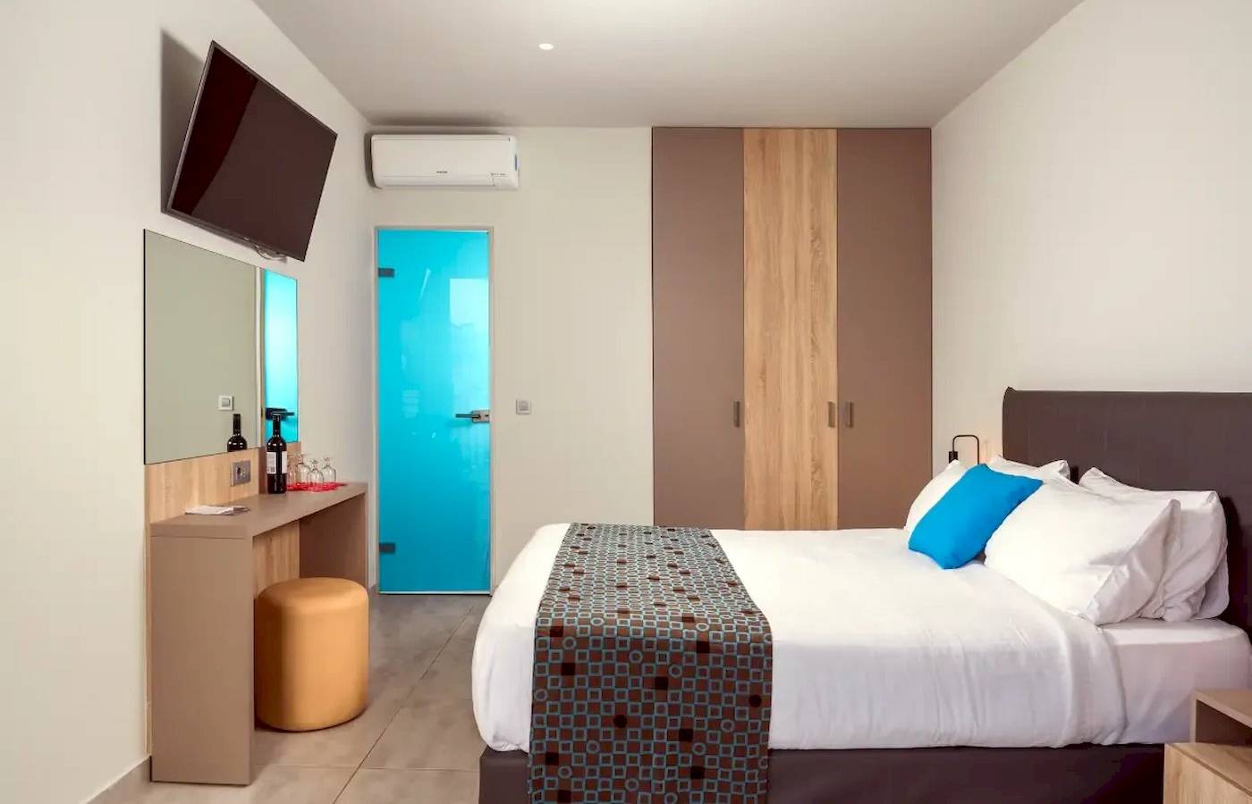 Innenansicht eines Zimmers im Corissia Beach Hotel mit einem Bett, einem Schreibtisch, einem Fernseher und einer Tür.