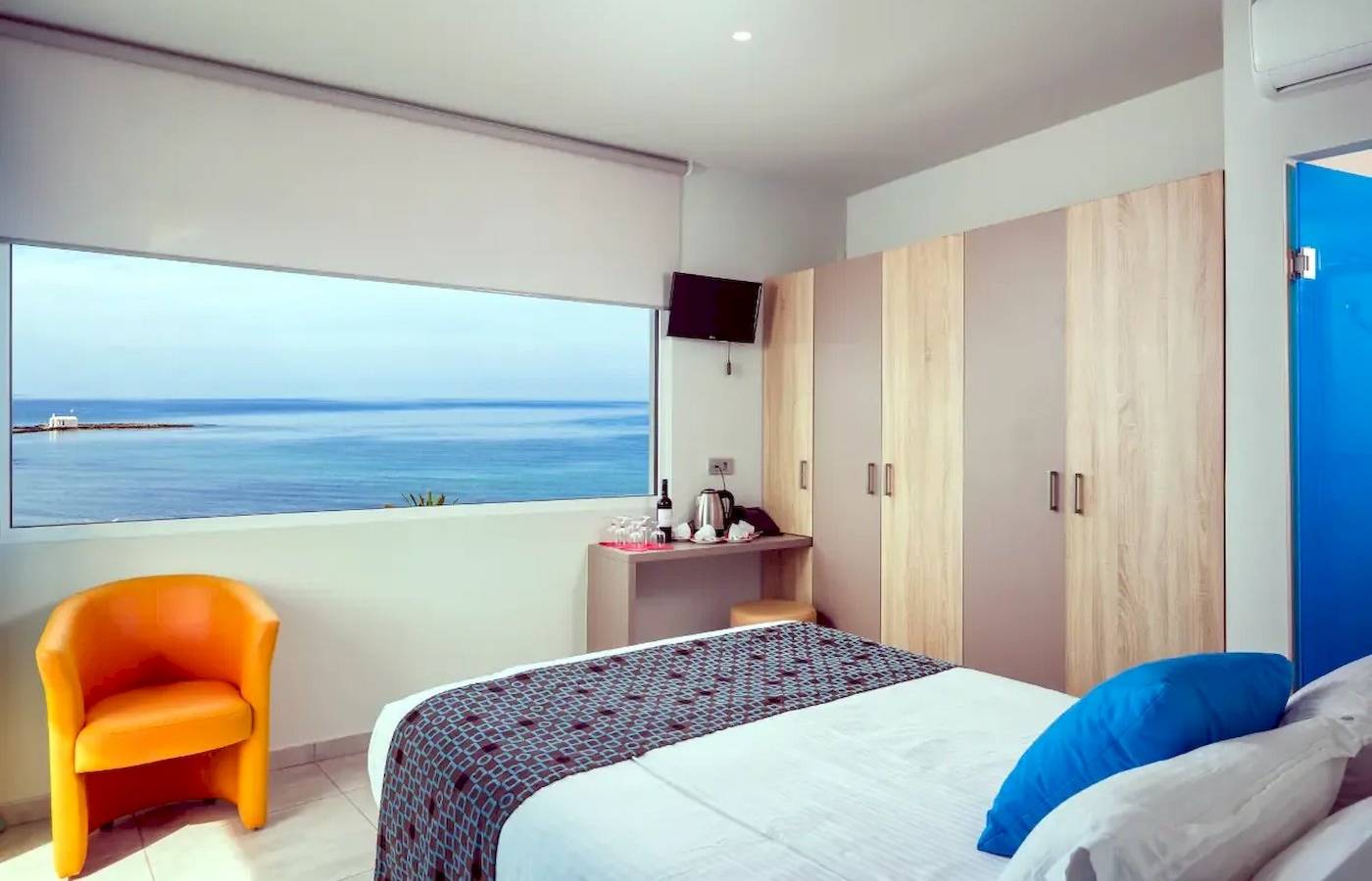 Zimmer im Corissia Beach Hotel mit Meerblick, Bett, oranger Stuhl, Fenster und Fernseher.