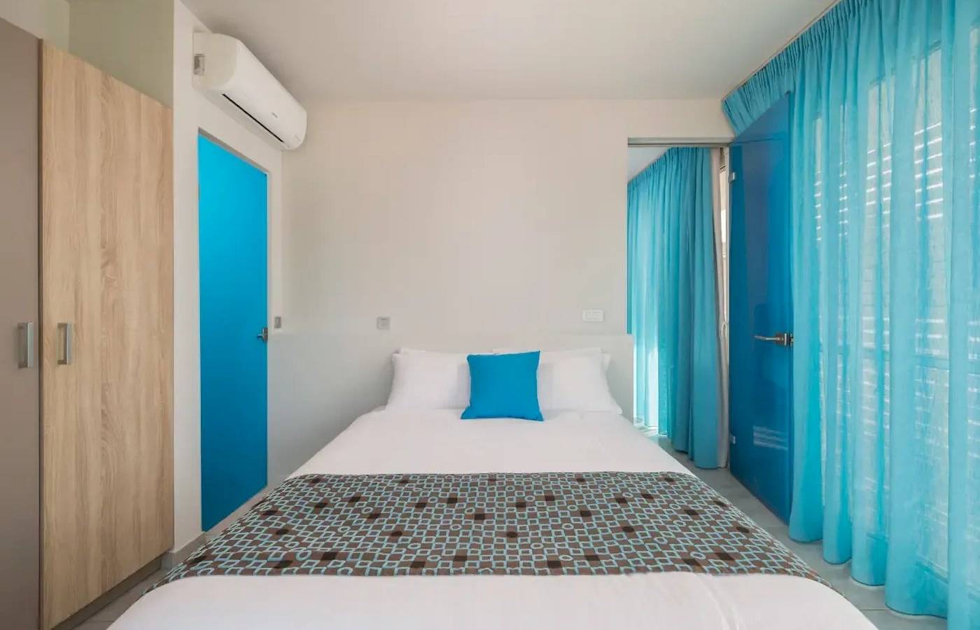 Schlafzimmer im Corissia Beach Hotel mit blauen Türen, einem Bett und einem blauen Kissen.