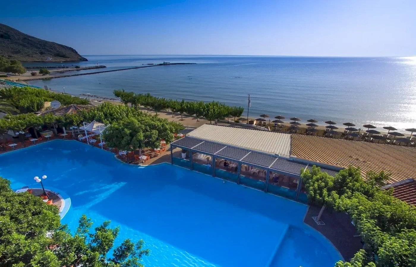 Luftaufnahme des Corissia Beach Hotels mit großem Swimmingpool, umgeben von Bäumen und Blick auf das Meer.
