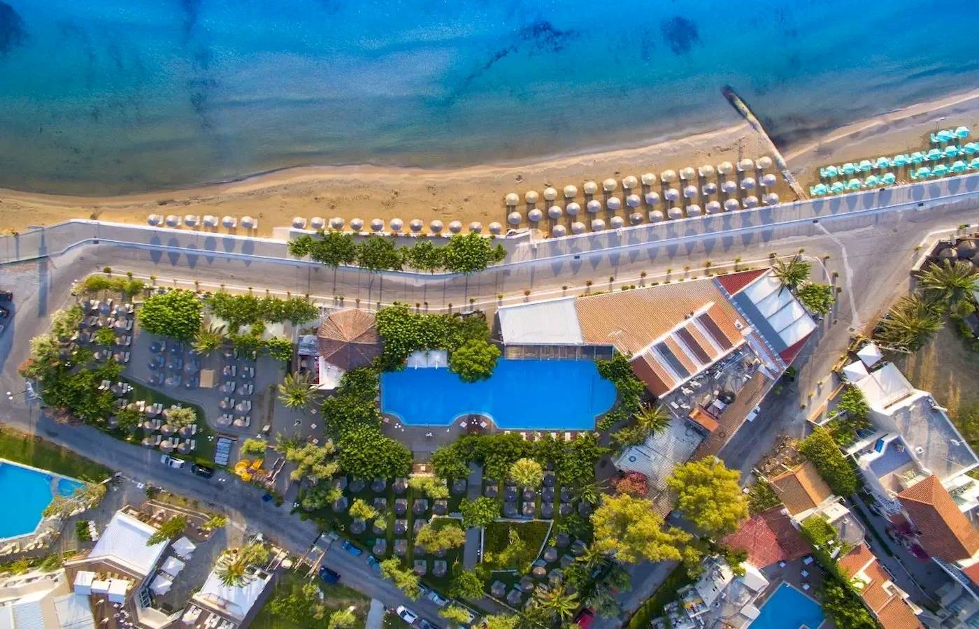 Luftaufnahme des Corissia Beach Hotels mit Blick auf den Strand, Pools und Sonnenschirme.