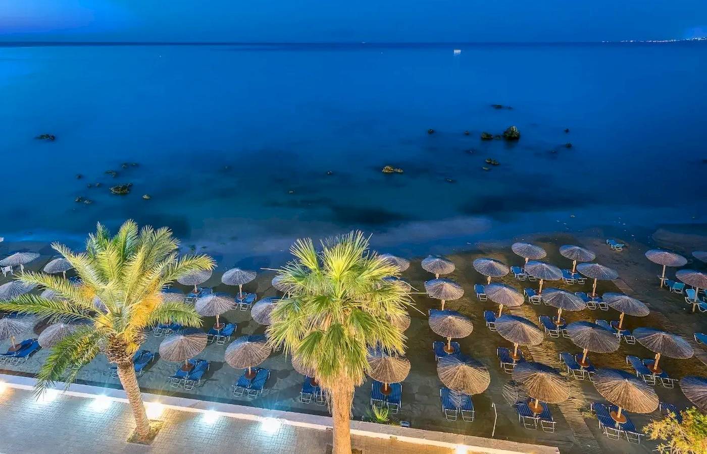 Abendblick auf den Strand des Corissia Beach Hotels mit vielen Sonnenschirmen und Liegen.