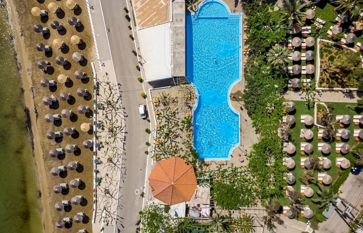 Luftaufnahme des Corissia Beach Hotels mit Swimmingpool, Sonnenschirmen und Liegen.