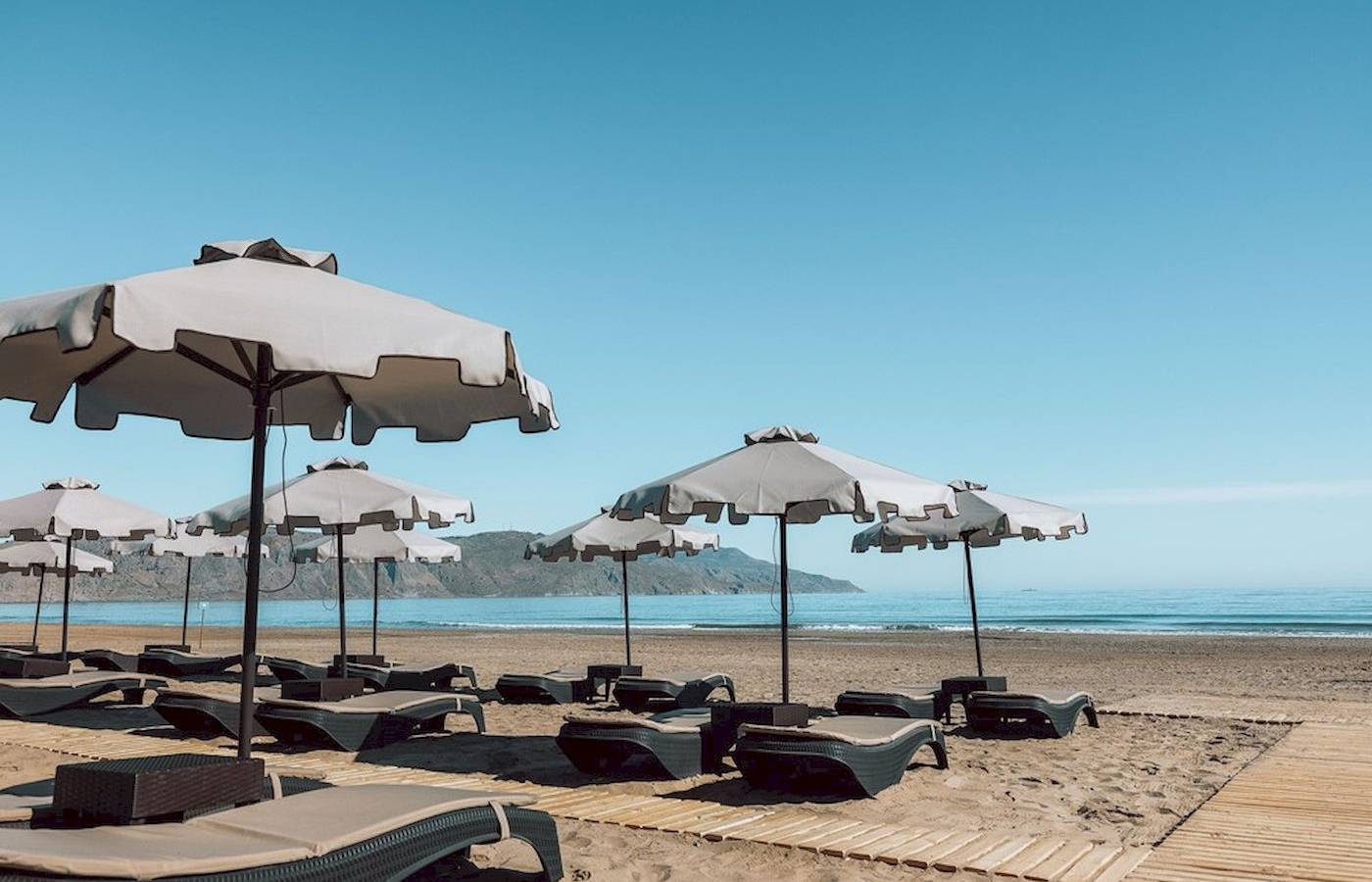 Eine Reihe von Sonnenliegen mit Sonnenschirmen auf dem Strand des Eliros Mare Hotels