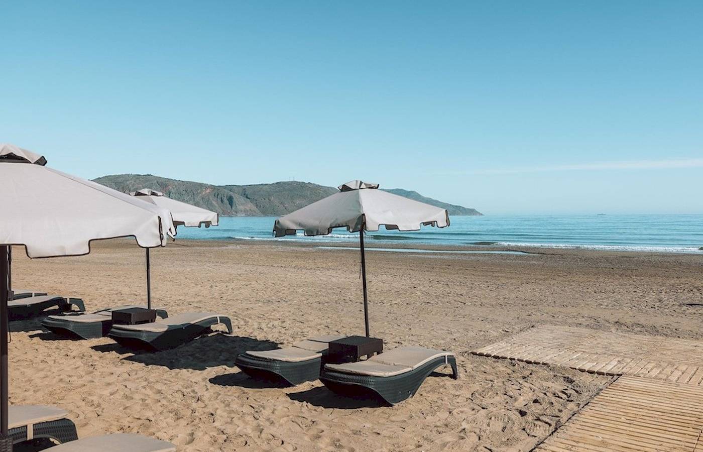 Eine Reihe von Sonnenliegen mit Sonnenschirmen auf dem Strand des Eliros Mare Hotels