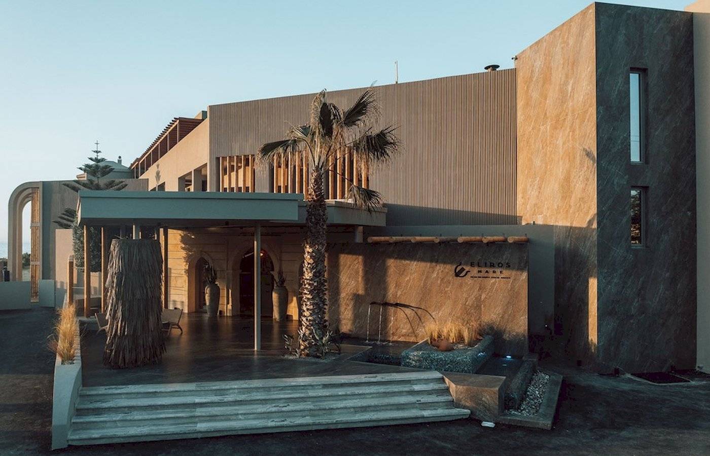 Außenansicht des Eliros Mare Hotels mit Eingang, Palme und Wasserbrunnen.