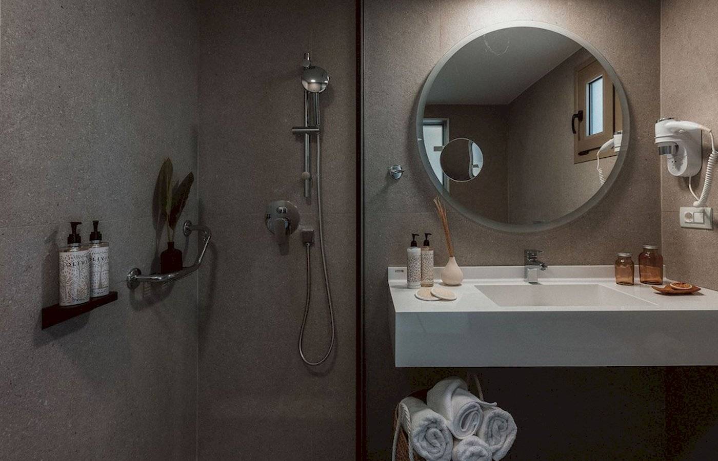 Badezimmer im Eliros Mare Hotel mit Dusche, Waschbecken und Handtüchern.