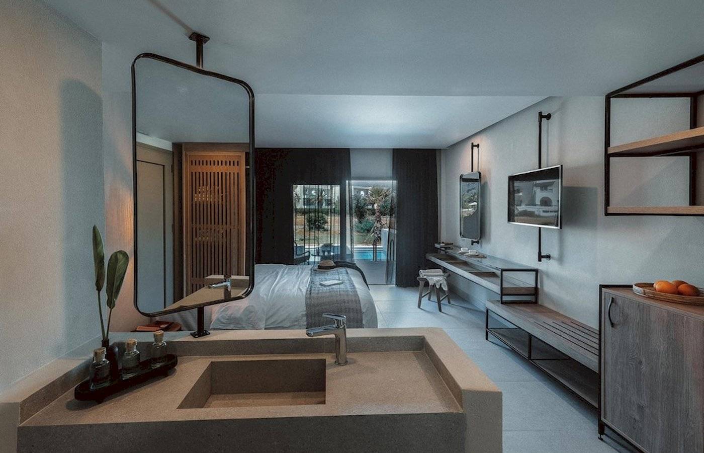 Innenansicht eines Zimmers im Eliros Mare Hotel mit Bett, Spiegel, Waschbecken und Pool im Hintergrund.