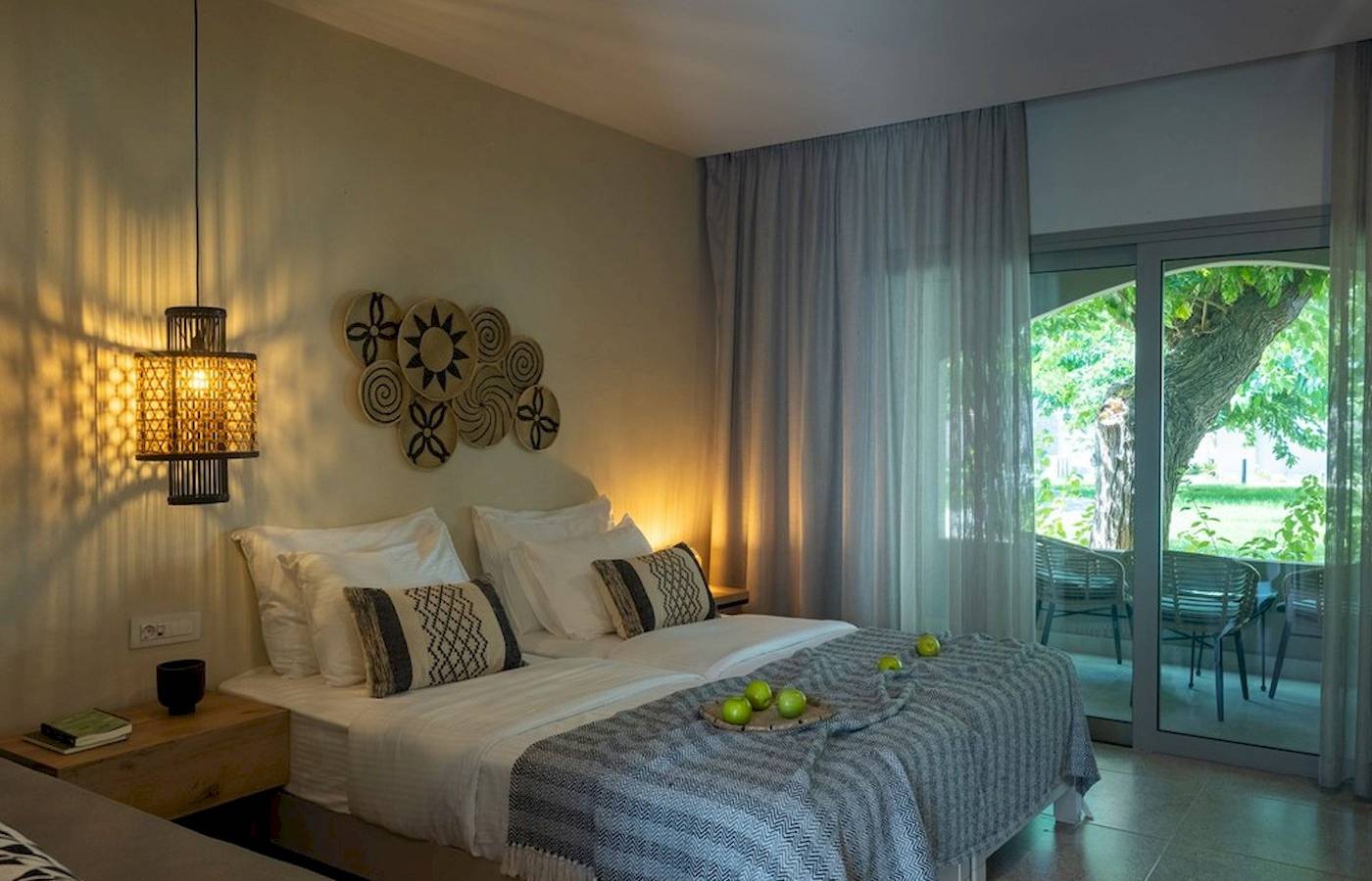 Schlafzimmer im Eliros Mare Hotel mit zwei Betten, Kissen, Bettwäsche, Lampen und offenem Balkon.