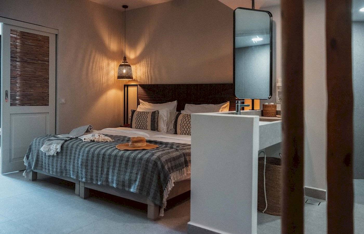 Schlafzimmer im Eliros Mare mit Bett, Decken, Kissen, Spiegel und Lampe.