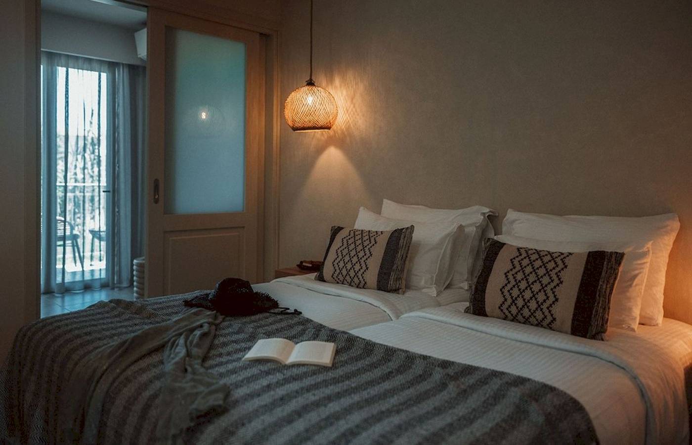 Doppelbettzimmer im Eliros Mare Hotel mit Bettwäsche, Kissen und einem offenen Buch auf der Bettdecke.