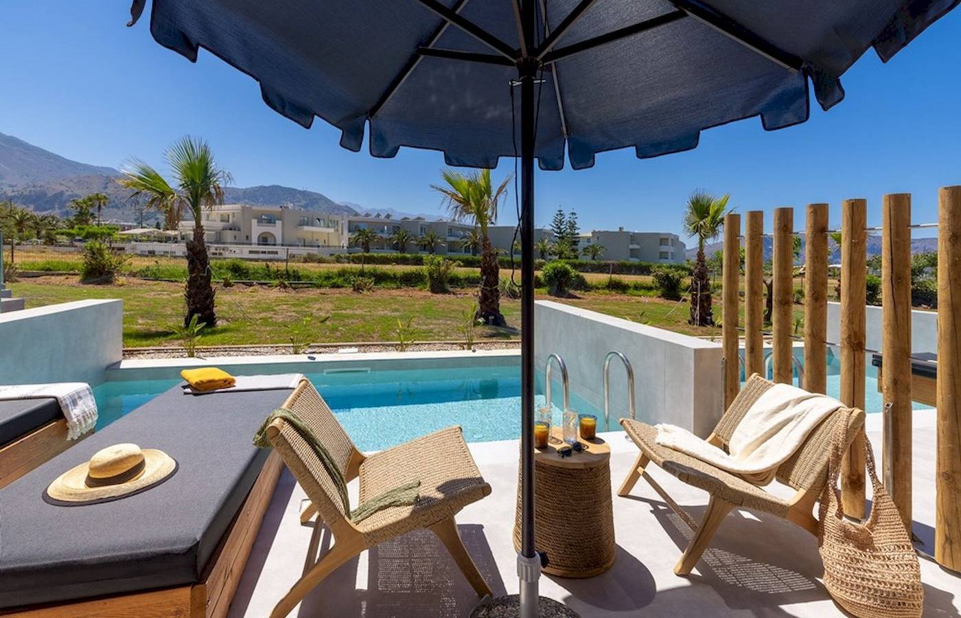 Außenbereich des Eliros Mare Hotels mit Pool, Liegen, Tisch und Sonnenschirm.