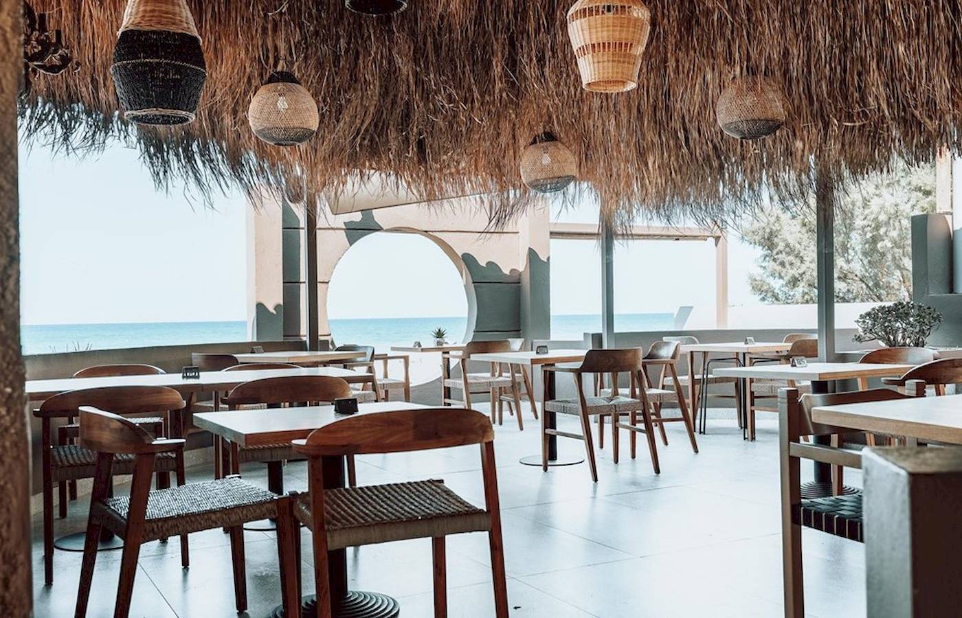 Innenansicht des Eliros Mare Hotels mit Blick auf das Meer, Tische und Stühle im Freien.