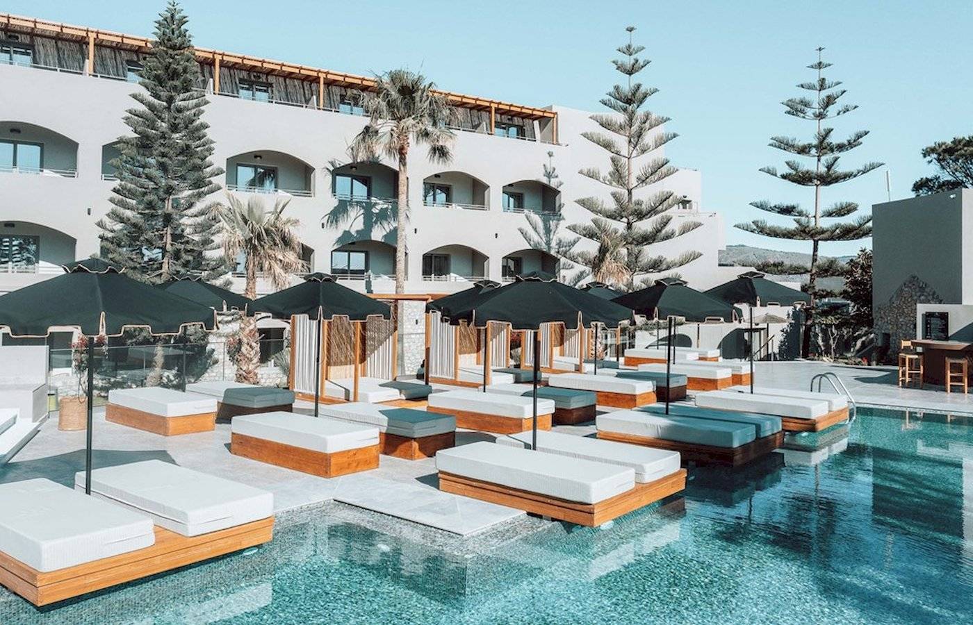 Pool-Lounge mit weißen Liegen und schwarzen Sonnenschirmen im Eliros Mare Hotel.