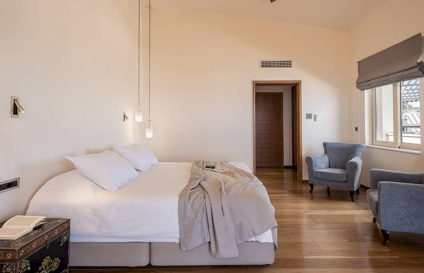 Schlafzimmer im Cretan Dream Resort & Spa mit großem Bett, Sesseln, Deckenventilator und Fenstern.