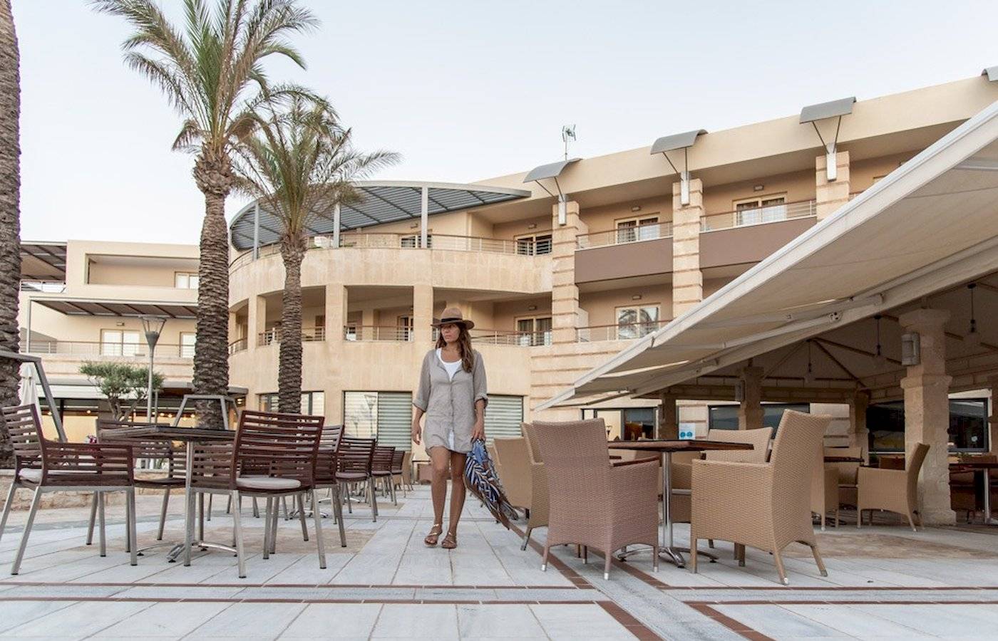 Frau im Sommerkleid und Hut geht vor dem Cretan Dream Resort & Spa entlang