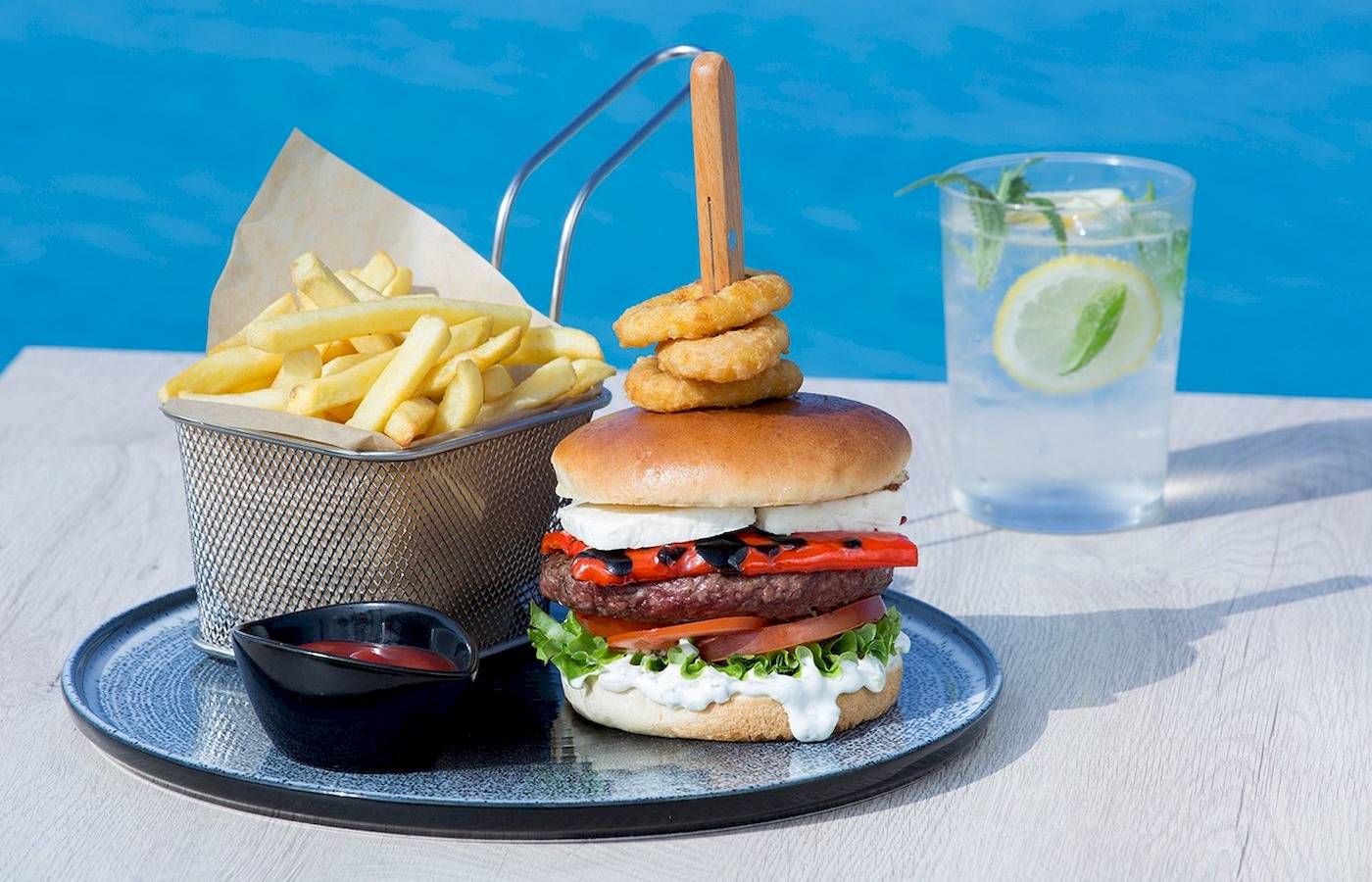 Ein Burger mit Pommes und Getränk am Pool des Cretan Dream Resort & Spa.