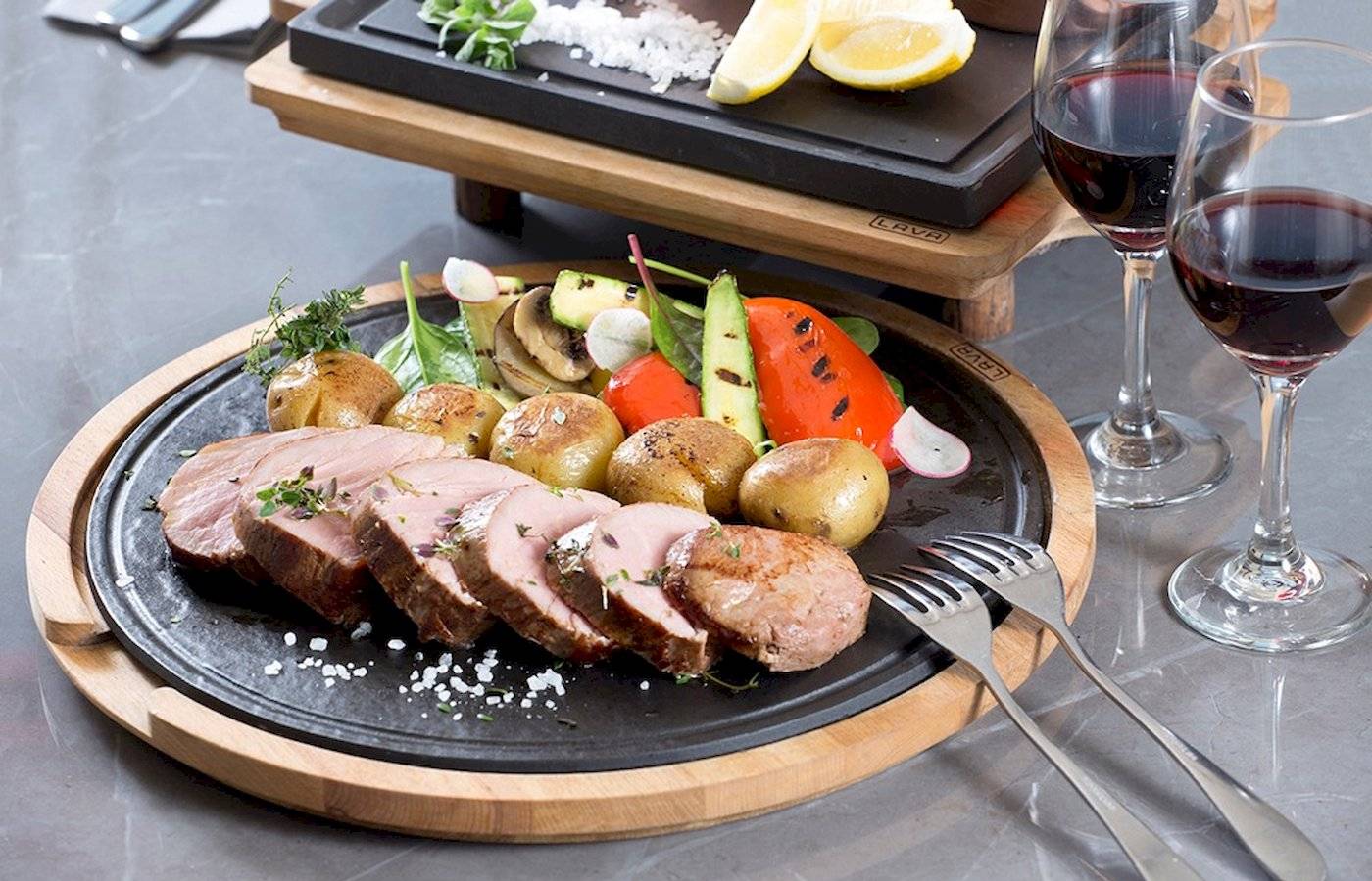 Fleischplatte mit Gemüse und zwei Weingläsern auf einem schwarzen Teller