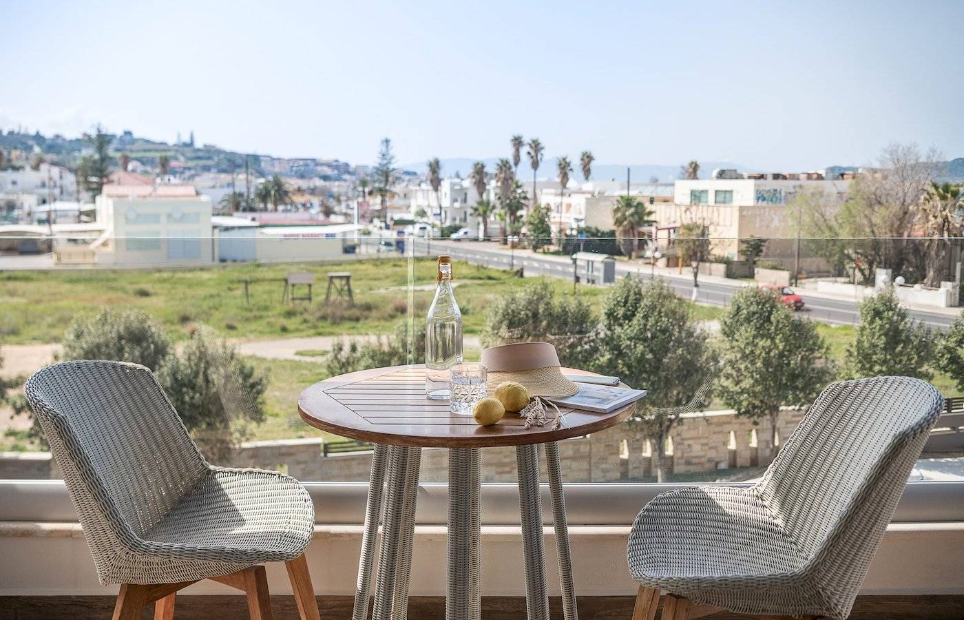 Zwei Stühle auf einem Balkon mit Aussicht auf eine Stadt, inklusive Tisch mit Flasche und Früchten.