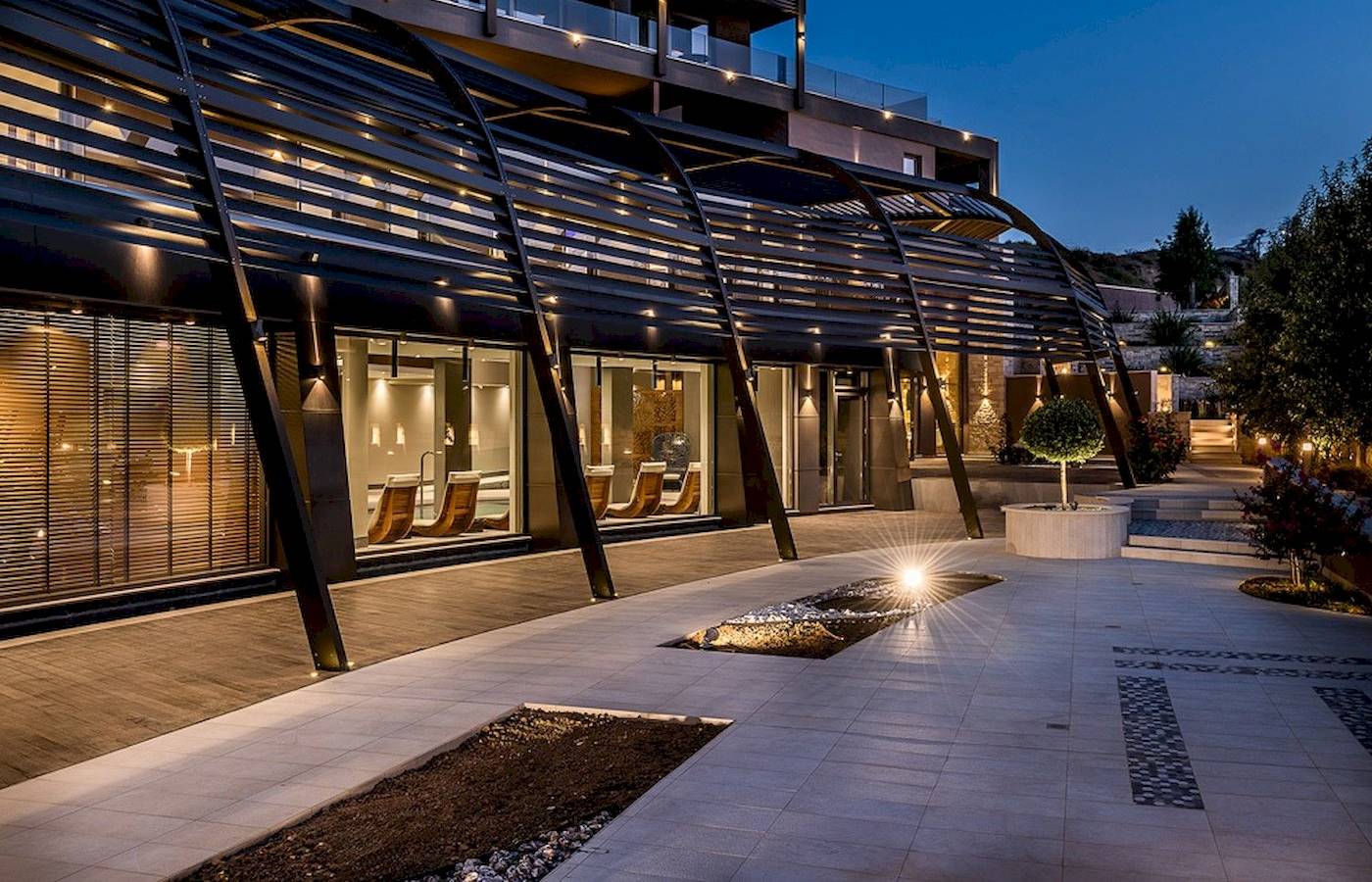 Die Außenansicht des Cretan Dream Resort & Spa bei Nacht mit einer gebogenen Pergola und beleuchteten Innenräumen.