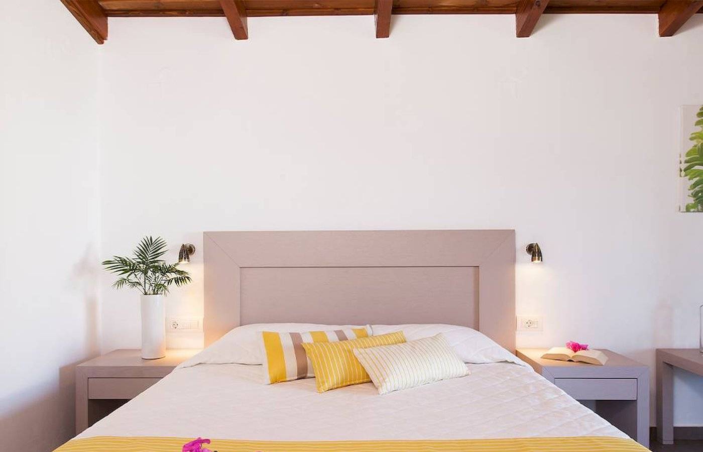 Schlafzimmer im Chrissi Amoudia Hotel mit gelben und weißen Bettwäsche, Blumen und Nachttischen.