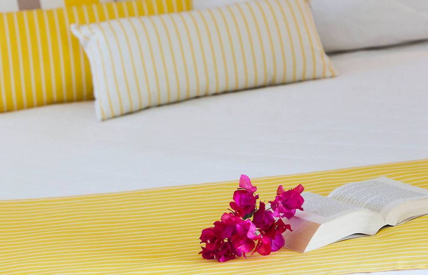 Foto von einem Bett im Chrissi Amoudia Hotel mit gelben Kissen und einer offenen Buch mit Blumen darauf.